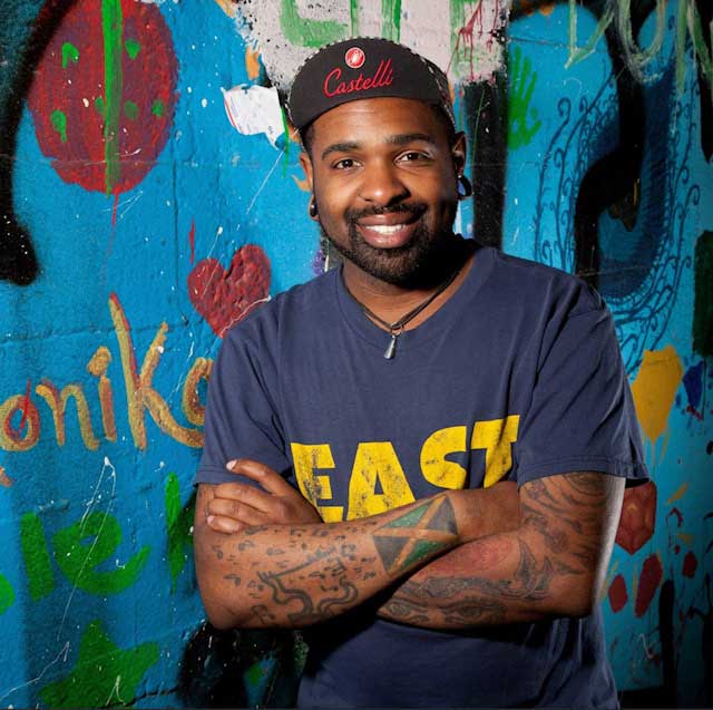 Rion F. Manning, standing with arms crossed in front of wall with graffiti