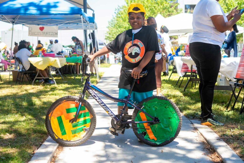 Young Black boy standing with bike decorated with orange and green duct tape.